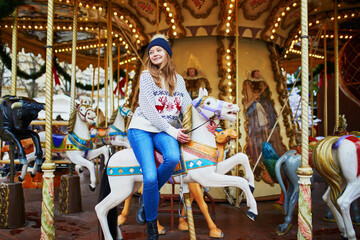 Fototapeta na wymiar Beautiful young woman riding a horse on merry-go-round on traditional Christmas market in Paris