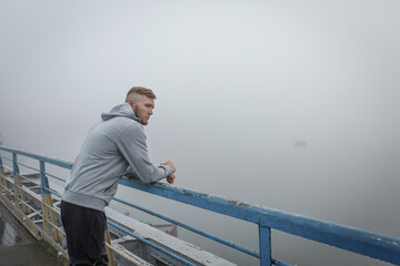 Man in gray hoodie stay on bridge in foggy morning