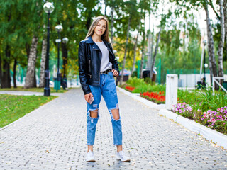 Young girl in a woolen sweater and torn jeans posing in an autumn park