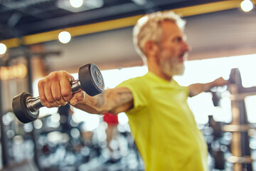 Fit over fifty. Side view of a mature caucasian man exercising with dumbbells at gym, focus on hand