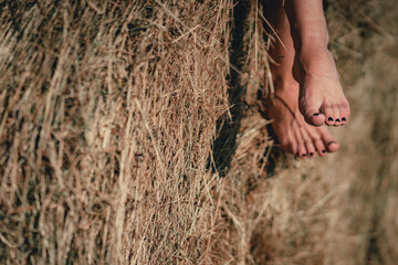 Bare feet, ankles of a young girl sitting on hay collected in large rolls
