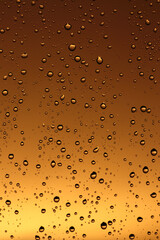 Rain drops on the window glass. Drops of water on window, yellow and orange sunset in background.