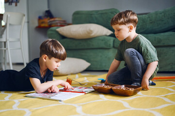 Two young preschool boys reading book and wathing pictures. Caucasian children plays at home. Kids eating snacks on the floor