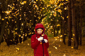 Laughing girl in a red jacket in the park against the background of falling autumn leaves.