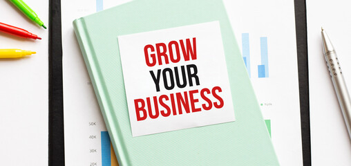 Financial diagram on white big notepad, green book and paper sheet with text GROW YOUR BUSINESS. Business concept