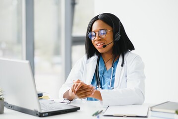 Smiling african american female doctor gp wears white medical coat using laptop computer at workplace gives remote online consultation, working on pc, consulting patient in internet telemedicine chat.