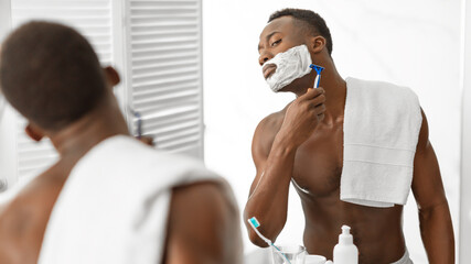 African Guy Shaving Face Covered With Shave Foam In Bathroom