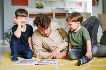 Father with sons reading book, spending time together at home and lying on the floor