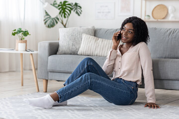 Obraz premium Home Pastime. Cheerful african lady woman talking on cellphone in living room