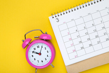 Fototapeta na wymiar Calendar page with alarm clock on yellow background