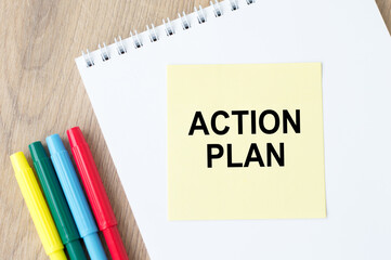 Action plan text on paper on notepad there are colored markers nearby on a wooden table. Business and finance concept