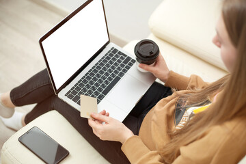 Young woman holding credit card and using laptop computer. Online shopping, e-commerce, internet banking, spending money, working from home concept
