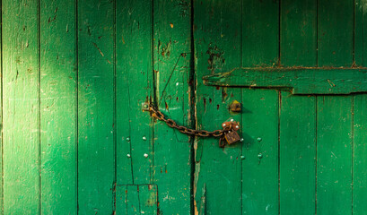 Old wooden green door with chain and padlock. Planks painted with green paint. Copy space. Entrance to the building