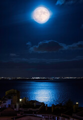 A Bright full moon lights up water over a city skyline