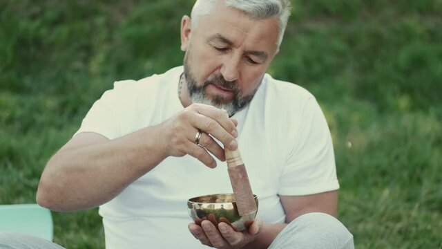Meditation cocncept. Man holding a bowl and a wooden stick sitting in a park