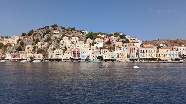 Rhodes, Greece: Pan shot of symi island with colorful house with a fisherman on boat with net catching fish for living