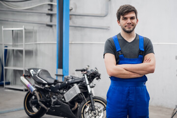 Fototapeta na wymiar A mechanic in uniform is standing near a motorcycle and looking at the camera
