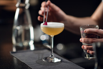 A glass with a bright yellow alcoholic cocktail on the bar and the hands of a bartender in a nightclub
