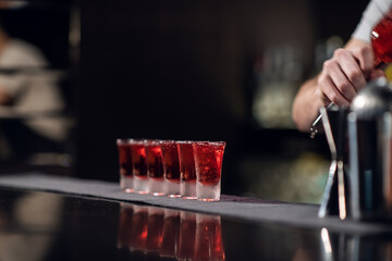bartender pours red alcohol into shots on the bar, bartender's show.
