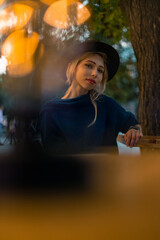 beautiful young lady portrait in evening street cafe patio outdoor table and blurred orange garland...