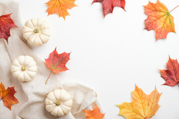 Autumn composition. Frame made of pumpkins, colorful maple leaves, beige fabric on white background. Flat lay, top view. Autumn fall, harvest, thanksgiving concept.