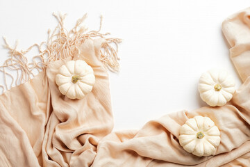 Beige scarf and pumpkins on white background. Autumn composition, flat lay, top view. Hygge, nordic, cozy style.