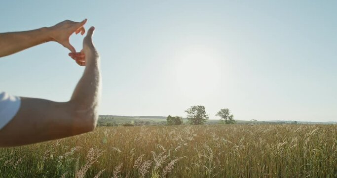 Young man in a hardhat visualising a new project as he stands overlooking an agricultural field of golden cereal making a frame gesture with his hands