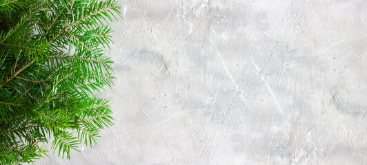 Christmas background with grey concrete structure and spruce branches without decoration on the right and empty space for text on the left. Top view of spruce branches on a gray stone surface. Banner