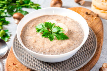 Mushroom cream soup. Champignon soup puree, toast and parsley on a gray concrete background. Tasty winter food, vegetarian food.