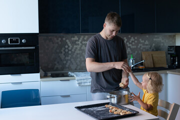 Young father and his small pretty daughter cooking together. Family is happily making cookies in the kitchen