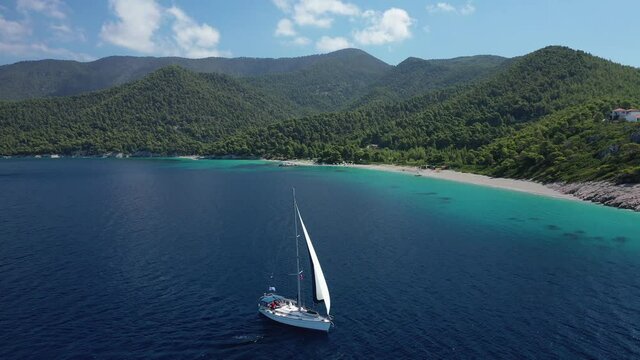 Aerial drone video of sailing boat cruising near famous turquoise paradise beach of Milia covered with pine trees, Skopelos island, Sporades, Greece