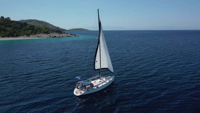 Aerial drone video of sailing boat cruising near famous turquoise paradise beach of Milia covered with pine trees, Skopelos island, Sporades, Greece