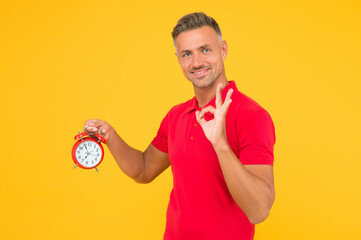 All right. Happy man hold alarm clock showing OK sign. Punctuality and accurate timekeeping....
