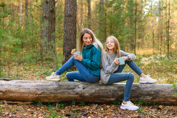 Fototapeta premium Mom and daughter have fun talking in the autumn forest. The girls are drinking tea at the picnic.