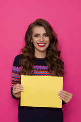 Smiling Woman In Sweater With Colorful Pattern Holds White Yellow Paper In Front Of Her