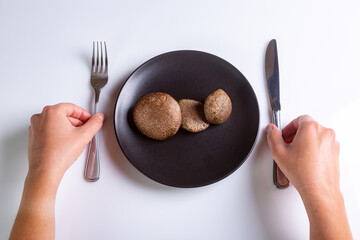 Raw Jersey cow mushrooms in a black plate and a knife and fork nearby on a white background top view. Human hands holding cutlery. Horizontal orientation. High quality photo
