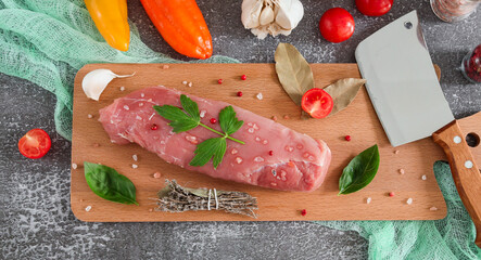 meat with vegetables
Pork fillet on a board with vegetables, herbs and a knife on a gray stone background, top view close-up.
