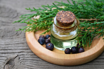 Juniper essential oil in a glass bottle on old wooden background. Herbal medicine, spa, aromatherapy and body care concept wit copy space.Selective focus.