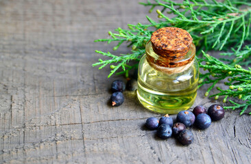 Juniper essential oil in a glass bottle on old wooden background. Herbal medicine, spa, aromatherapy and body care concept wit copy space.Selective focus.