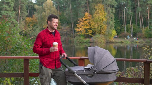Handsome man in red shirt with baby carriage in the park 