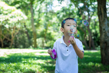 A little Asian boy blowing bubbles, playing with joy and happiness in the beautiful and green nature.