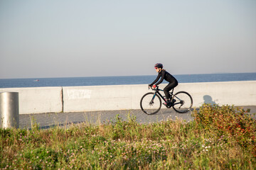 Fototapeta na wymiar A woman athlete rides a bicycle along the embankment in the morning at dawn. Outdoor exercise