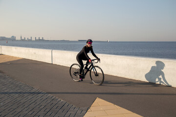 A woman rides a bicycle along the embankment. Riding a bicycle. Outdoor sports. Embankment of the...