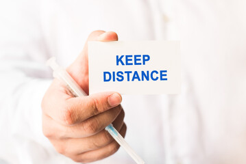 Word keep distance on a white background with a syringe in hand. Medicine concept