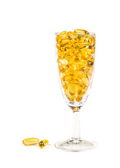 Transparent wine glass with fish oil orange yellow softgels capsules fish oil omega 3 or omega 6, omega 9, vitamin A, vitamin D, vitamin E isolated on white background. Healthy eating concept