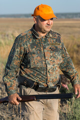 Duck hunter with shotgun walking through a meadow.