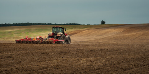 agricultural industrial landscape. a modern tractor with a trailed cultivator works on a hilly...