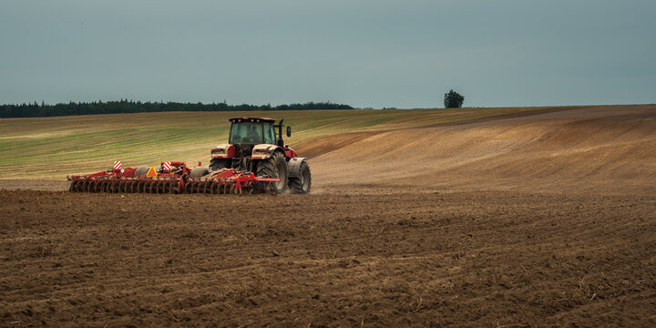 agricultural industrial landscape. a modern tractor with a trailed cultivator works on a hilly field before the autumn sowing campaign