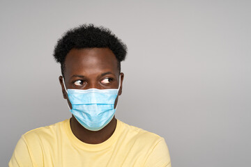 Serious Afro-American man in yellow t-shirt wear face mask looking away at copy space for advertising, offering, product, promotion text, sale, over studio gray background. Covid-19. 