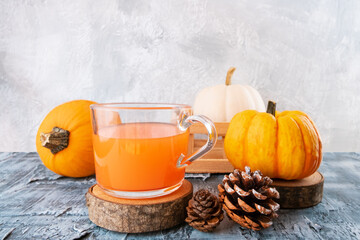 Pumpkin Orange color tea in glass cup on wooden stand with pumpkins around. Autumn still life with beverage for Halloween and Thanksgiving.